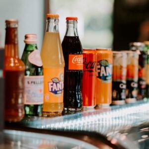 Close-up of assorted bottles and cans of soft drinks, including Coca-Cola and Fanta, on a reflective surface.